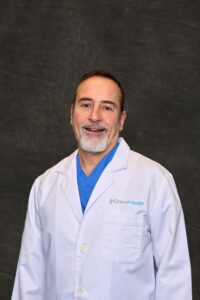 A professional headshot of Enrico Ascani, a man with a friendly smile, wearing a white medical coat.