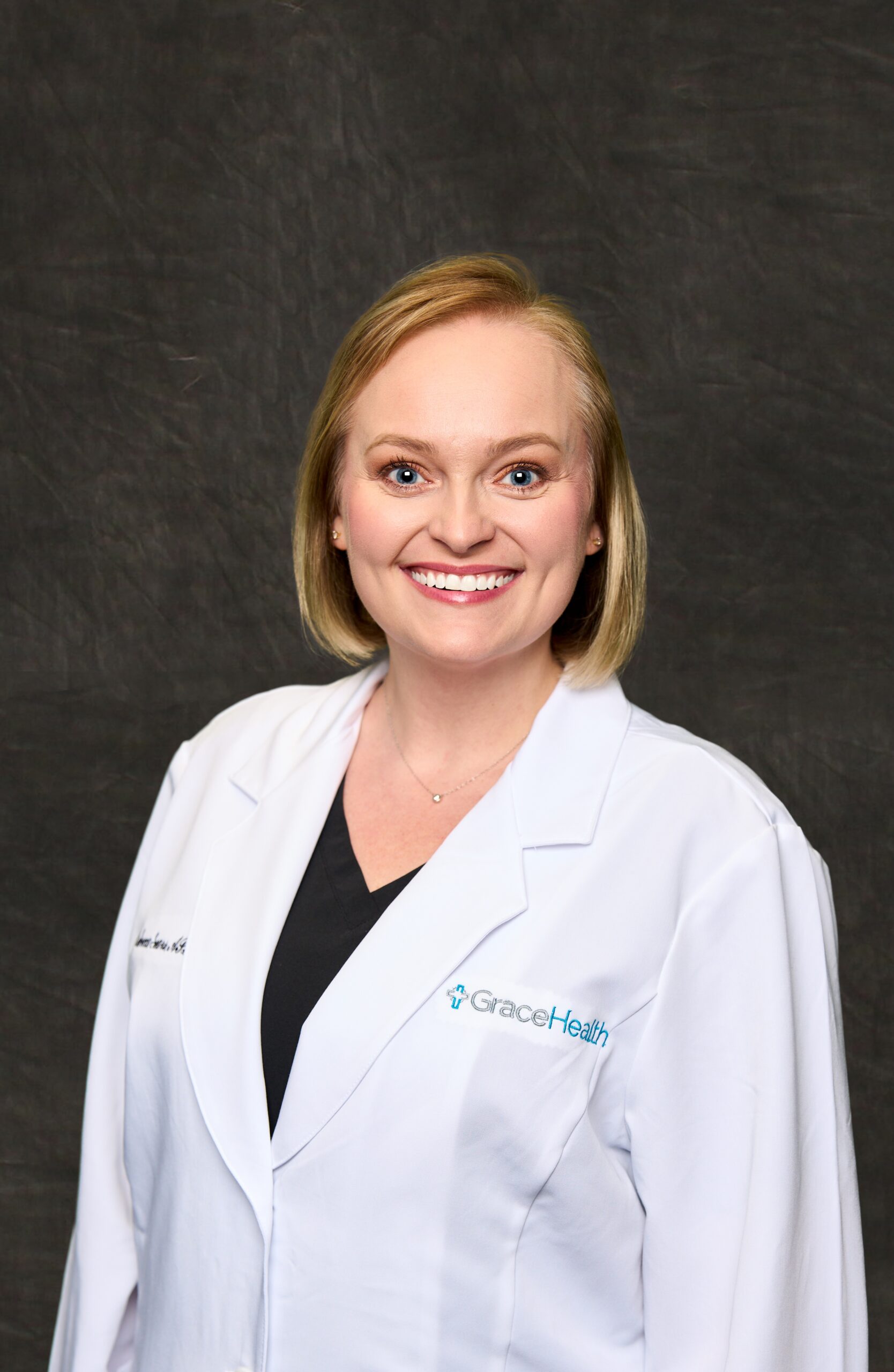 A professional headshot of Rebecca Sears, a blonde woman with short hair and a bright smile, wearing a white medical coat.