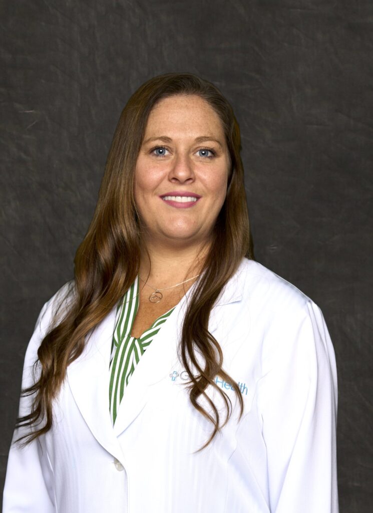A professional headshot of Valarie Roberts, a woman with long brown hair and a friendly smile, wearing a green and white shirt and a white medical coat.
