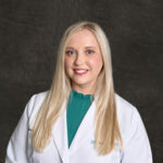 A professional headshot of Renzee Jarvis, a young blonde woman smiling, wearing a white pharmacist's coat over a teal blouse.